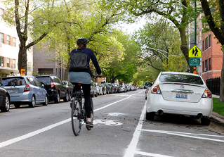 A person rides a bicycle in a striped bike lane on a residential street
