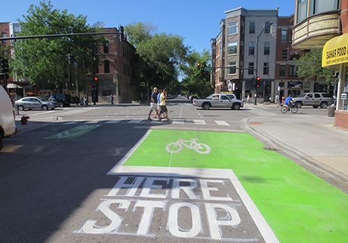 Street with green painted bike lane and bike symbol leading up to signalized intersection