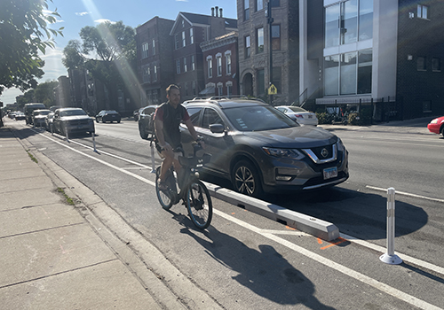A person rides a bike in a bike lane between the curb a parking lane with concrete barrier separation