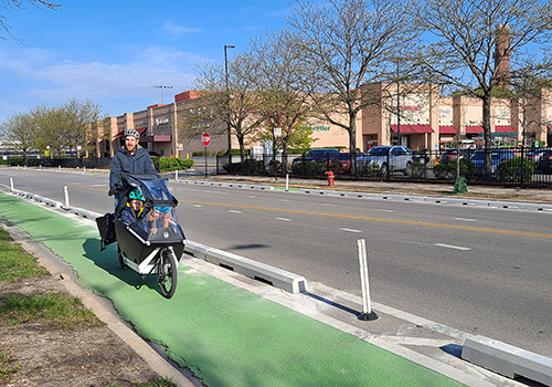 Adult and two children riding a cargo bike on a bike lane painted green, separated from the vehicle travel lane by a low concrete barrier and plastic bollards