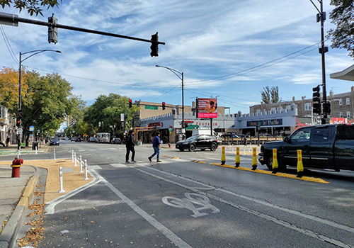 View of intersection with bollards installed along  and rubber speed bump on both sides of crosswalk.