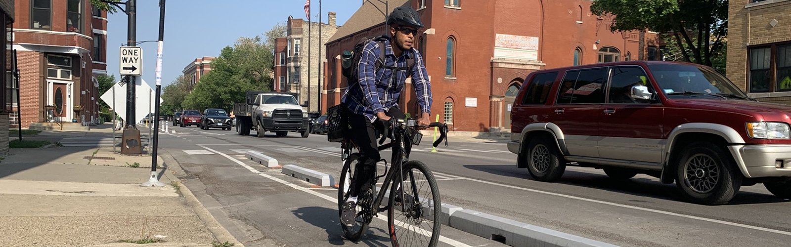 Person riding bike towards viewer on roadway in bike lane with concrete curbs separating bike lane from vehicle travel lane.