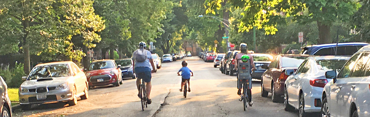 Adult, child, and adult with child on the back of the bike in a seat riding bikes on a street