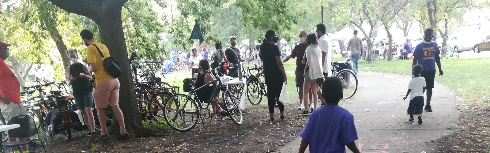 Kid walking away from viewer on sidewalk through park with bikes parked on grass
