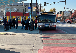 CTA bus pulled over at curbside stop in red bus only lane with a line of people waiting to board.