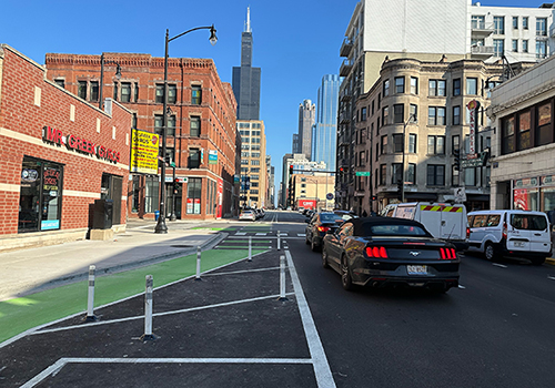 Person biking towards viewer in green painted bike lane separated from vehicle travel lane by concrete curb.