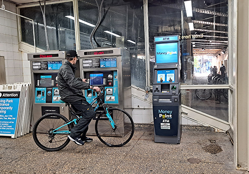 Interior of CTA rail station with person holding bike and paying for CTA fare at kiosk