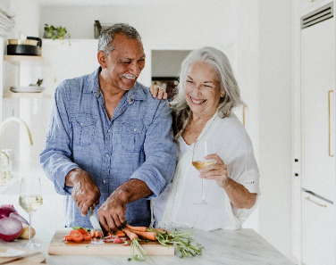older couple smiling and cooking together in kitchen