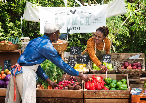A smiling man and woman stocking produce at a farmers' market booth