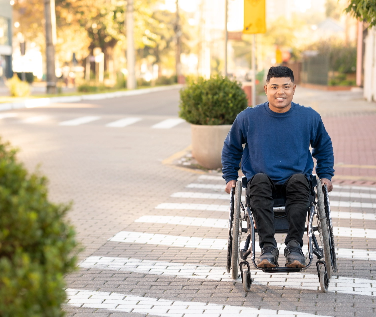 A young man in wheelchair crossing street in crosswalk